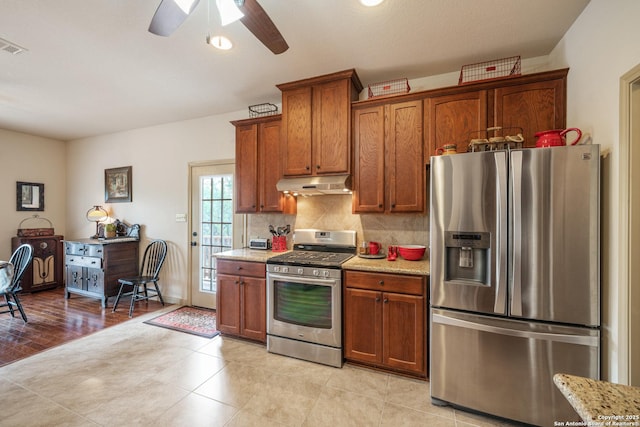 kitchen with decorative backsplash, ceiling fan, appliances with stainless steel finishes, brown cabinets, and under cabinet range hood