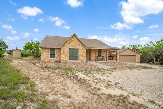 single story home featuring a porch, driveway, a storage shed, an outdoor structure, and stone siding