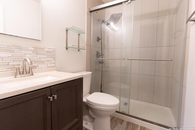 bathroom featuring toilet, a stall shower, backsplash, and vanity