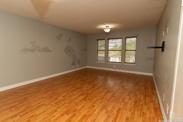 empty room with a textured ceiling, baseboards, and light wood-type flooring