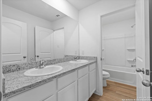 full bath featuring toilet, double vanity, a sink, and wood finished floors