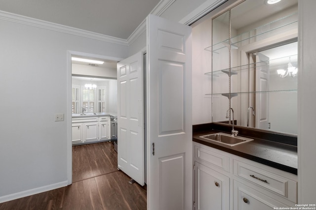 bar featuring a sink, a notable chandelier, crown molding, wet bar, and dark wood finished floors