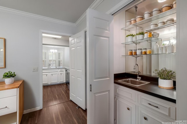 bar featuring a sink, dark wood-style floors, baseboards, ornamental molding, and a notable chandelier