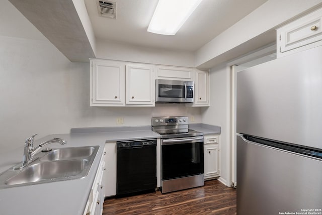 kitchen with white cabinetry, a sink, appliances with stainless steel finishes, light countertops, and dark wood-type flooring
