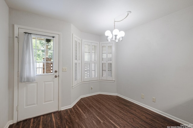 unfurnished dining area featuring an inviting chandelier, dark wood-style flooring, and baseboards