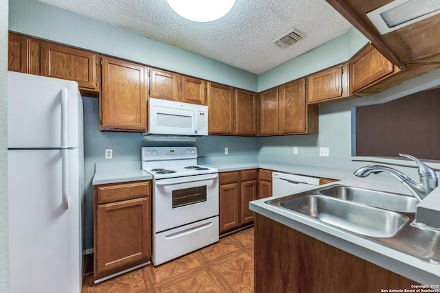 kitchen featuring white appliances, brown cabinetry, light countertops, a sink, and a textured ceiling