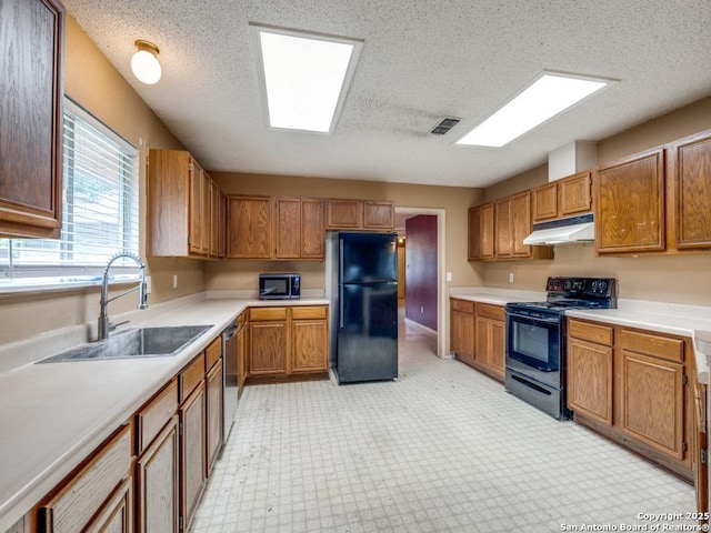 kitchen featuring a sink, under cabinet range hood, black appliances, light countertops, and light floors
