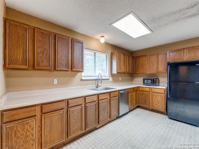 kitchen with stainless steel dishwasher, a sink, freestanding refrigerator, and brown cabinetry