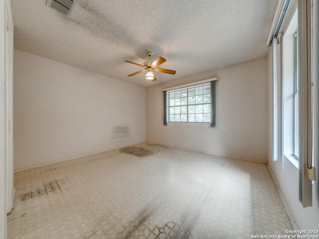 spare room featuring a textured ceiling, visible vents, a ceiling fan, and baseboards