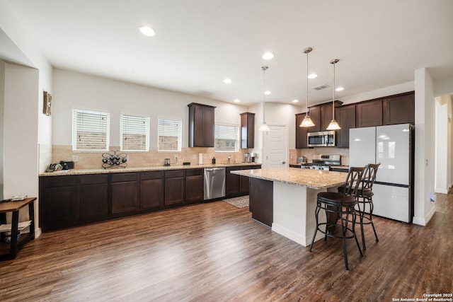 kitchen with appliances with stainless steel finishes, dark brown cabinets, a center island, dark wood finished floors, and backsplash