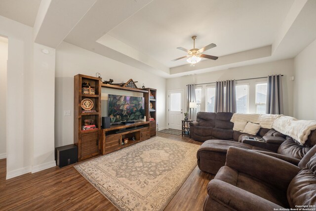 living room with dark wood-type flooring, a ceiling fan, baseboards, and a tray ceiling