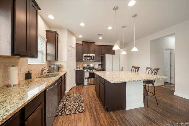 kitchen with a sink, dark wood-style flooring, a kitchen breakfast bar, dark brown cabinetry, and appliances with stainless steel finishes