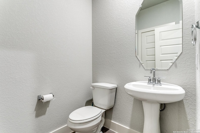 half bath featuring baseboards and toilet