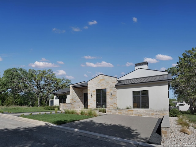 modern home with metal roof, a standing seam roof, stone siding, and stucco siding