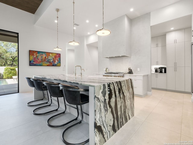 kitchen featuring pendant lighting, white cabinetry, modern cabinets, light stone countertops, and an island with sink