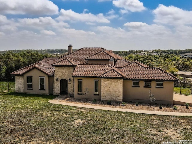 mediterranean / spanish-style house featuring a chimney, stucco siding, a tile roof, stone siding, and a front lawn