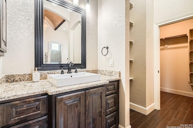 bathroom with baseboards, wood finished floors, a walk in closet, and a textured wall