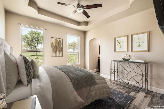 bedroom with baseboards, arched walkways, wood finished floors, and a raised ceiling