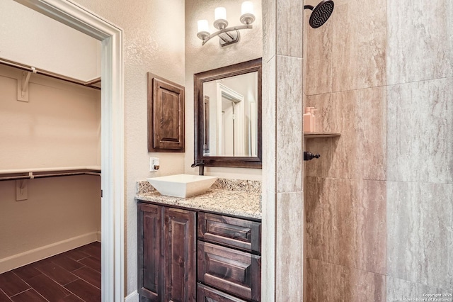 bathroom featuring a spacious closet, tiled shower, wood finished floors, and vanity