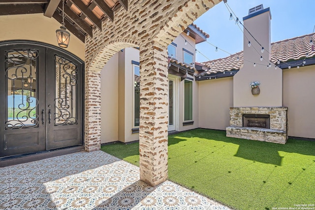 entrance to property featuring french doors, stucco siding, an outdoor stone fireplace, and a tiled roof