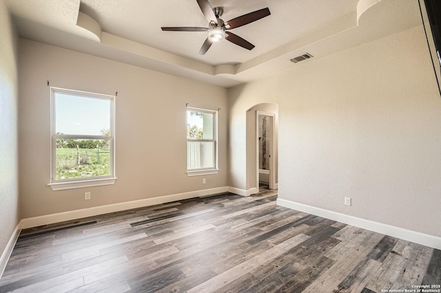 spare room with wood finished floors, visible vents, plenty of natural light, and arched walkways