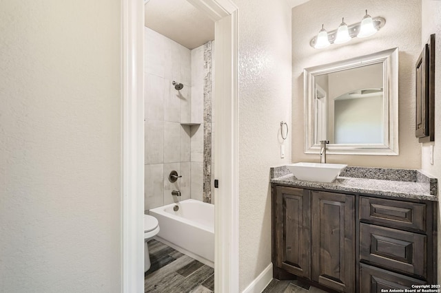 bathroom featuring vanity, toilet, a textured wall, wood finished floors, and  shower combination