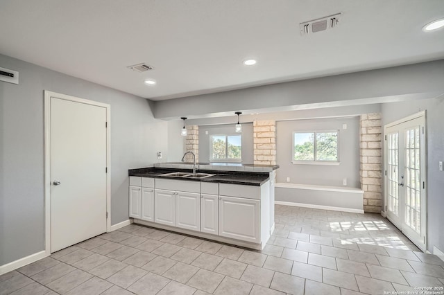 kitchen with a sink, visible vents, a peninsula, dark countertops, and white cabinets