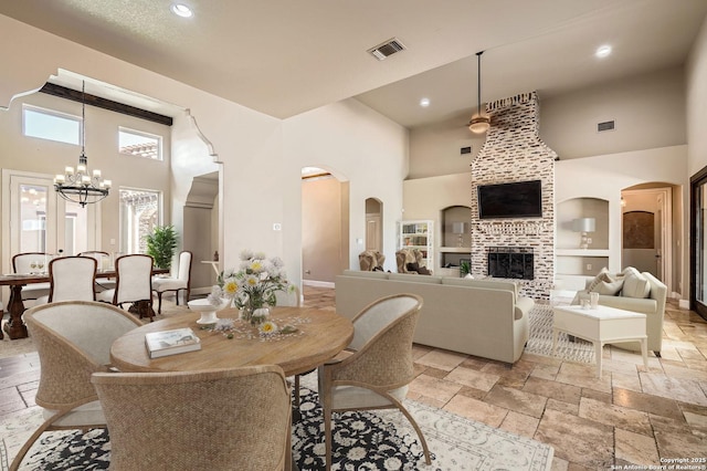 dining area featuring stone tile floors, visible vents, a chandelier, a high ceiling, and built in shelves