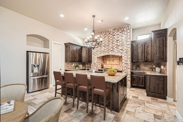 kitchen with dark brown cabinetry, visible vents, stone tile flooring, and stainless steel fridge with ice dispenser