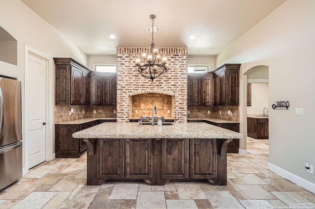 kitchen with a sink, stone tile flooring, a notable chandelier, visible vents, and freestanding refrigerator
