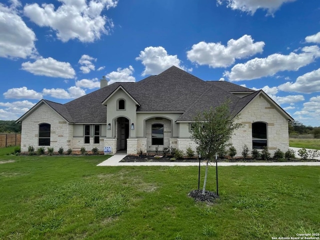 french country home with roof with shingles, a chimney, a front lawn, and stone siding
