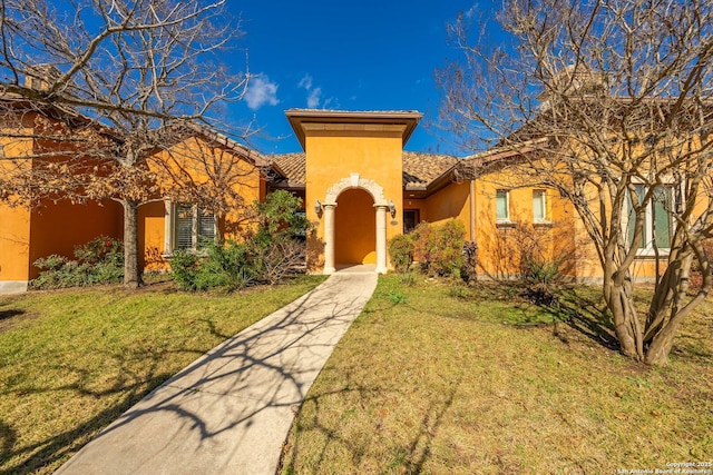 mediterranean / spanish house with stucco siding, a tiled roof, and a front lawn