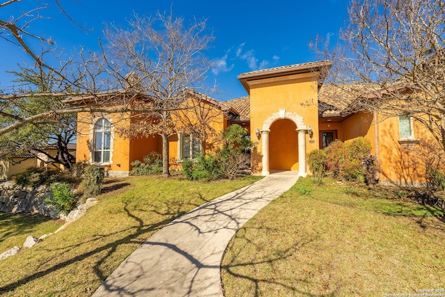 mediterranean / spanish house with stucco siding, a tiled roof, and a front yard