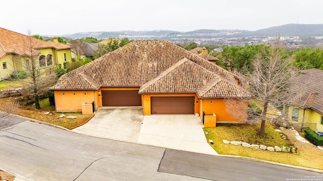 view of front of house with concrete driveway, a tiled roof, a mountain view, an attached garage, and stucco siding