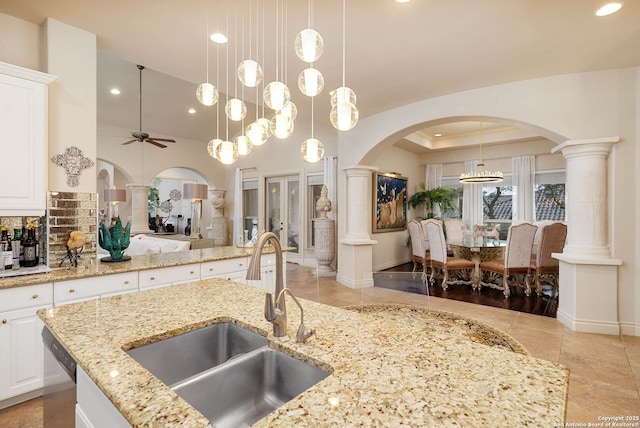 kitchen featuring arched walkways, hanging light fixtures, a sink, ornate columns, and a ceiling fan