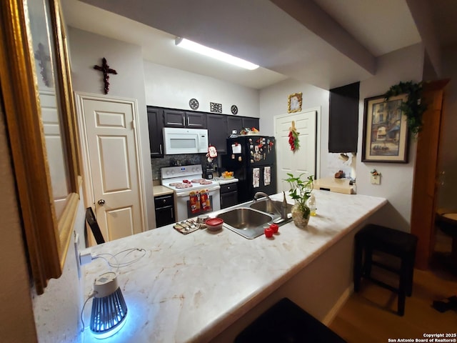 kitchen with white appliances, light countertops, dark cabinetry, a sink, and a peninsula
