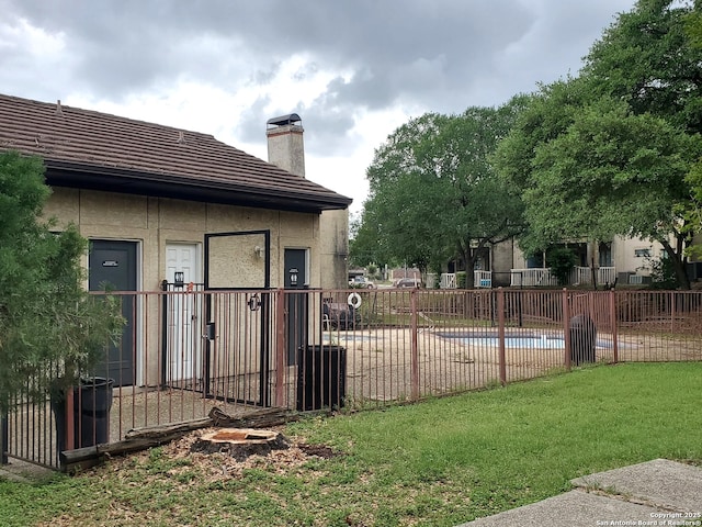 exterior space featuring a community pool, a chimney, stucco siding, a lawn, and fence