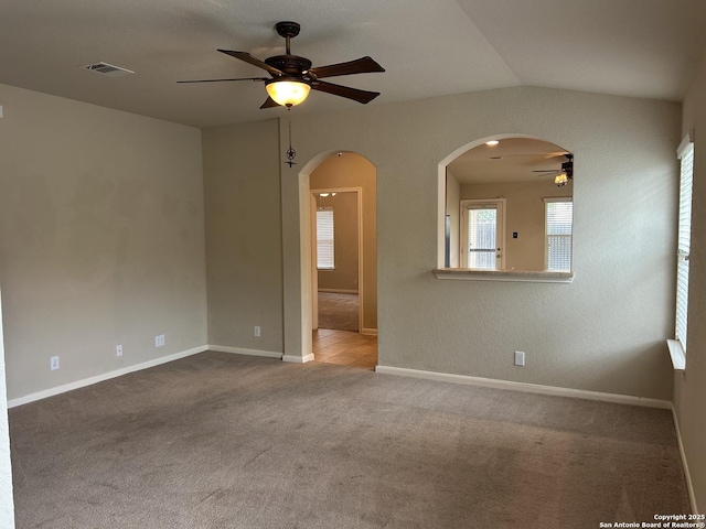 empty room featuring a ceiling fan, visible vents, baseboards, arched walkways, and carpet floors