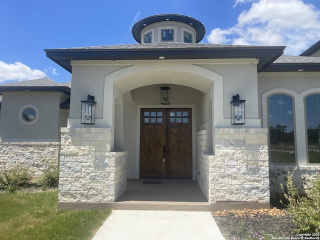 entrance to property with stucco siding, roof with shingles, and stone siding