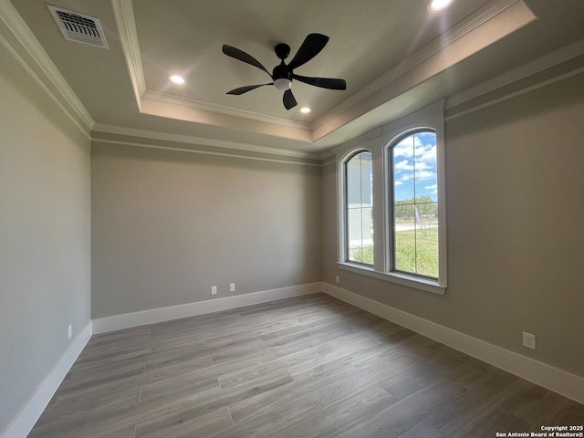 empty room featuring ceiling fan, a tray ceiling, visible vents, ornamental molding, and wood finished floors