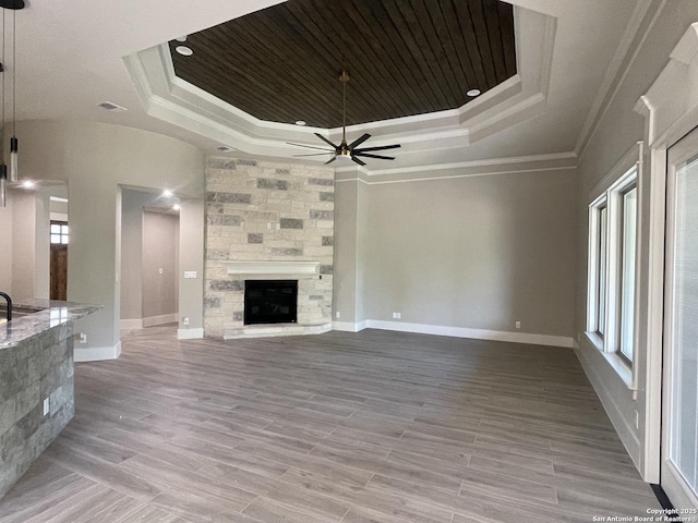 unfurnished living room with a raised ceiling, ceiling fan, a fireplace, and crown molding