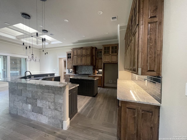 kitchen featuring light stone countertops, a sink, decorative backsplash, ornamental molding, and a large island with sink