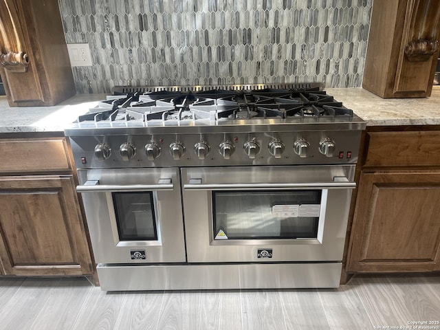 details with range with two ovens, light stone countertops, and light wood finished floors