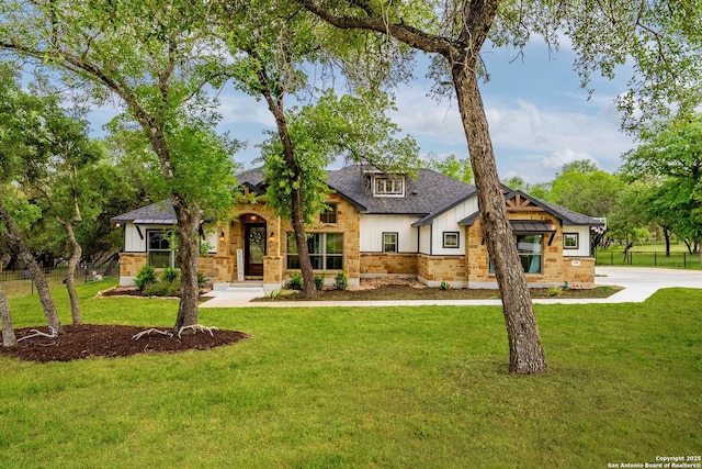 view of front facade with a front lawn, stone siding, board and batten siding, roof with shingles, and fence