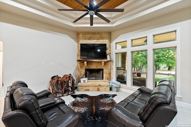 living room featuring wood ceiling, ceiling fan, a tray ceiling, and a stone fireplace