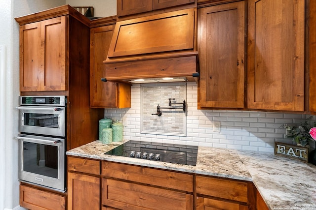 kitchen featuring tasteful backsplash, light stone countertops, stainless steel double oven, brown cabinetry, and black electric cooktop