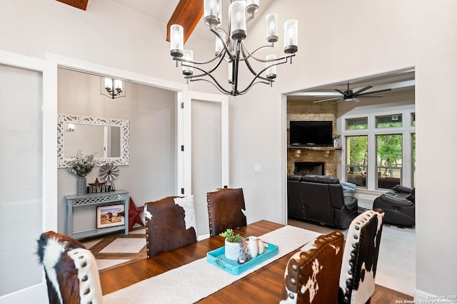 dining area featuring wood finished floors, a stone fireplace, and ceiling fan with notable chandelier