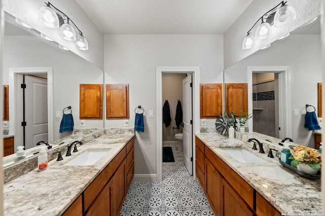full bath featuring two vanities, walk in shower, toilet, and a sink