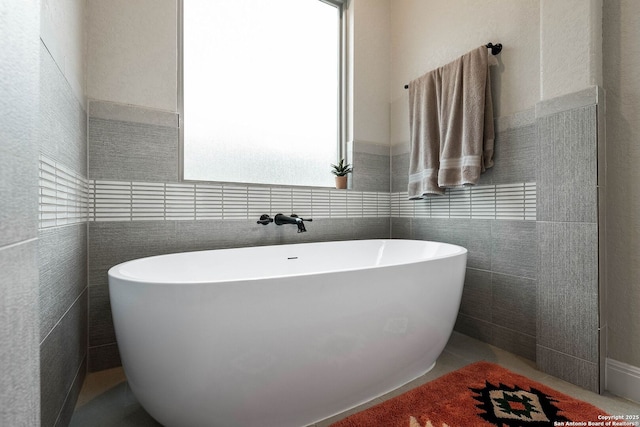 bathroom featuring tile walls, a freestanding tub, and wainscoting
