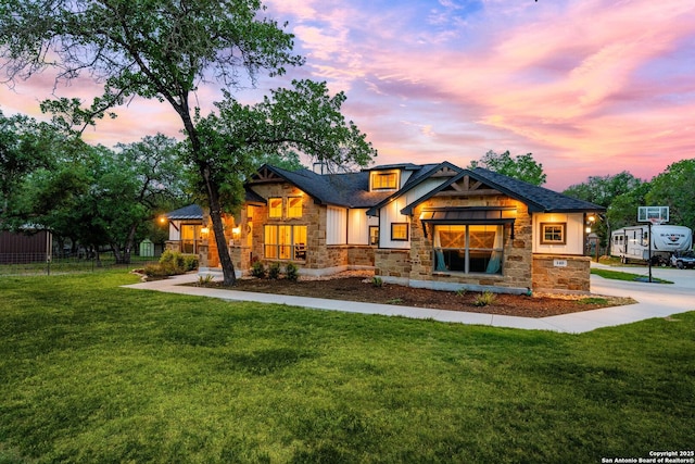 rear view of house with a lawn, fence, and stone siding